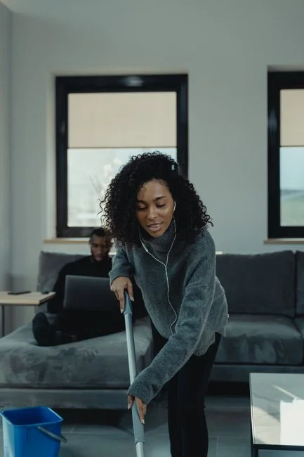 A professional cleaner in protective gear vacuuming the floor in a modern living room.